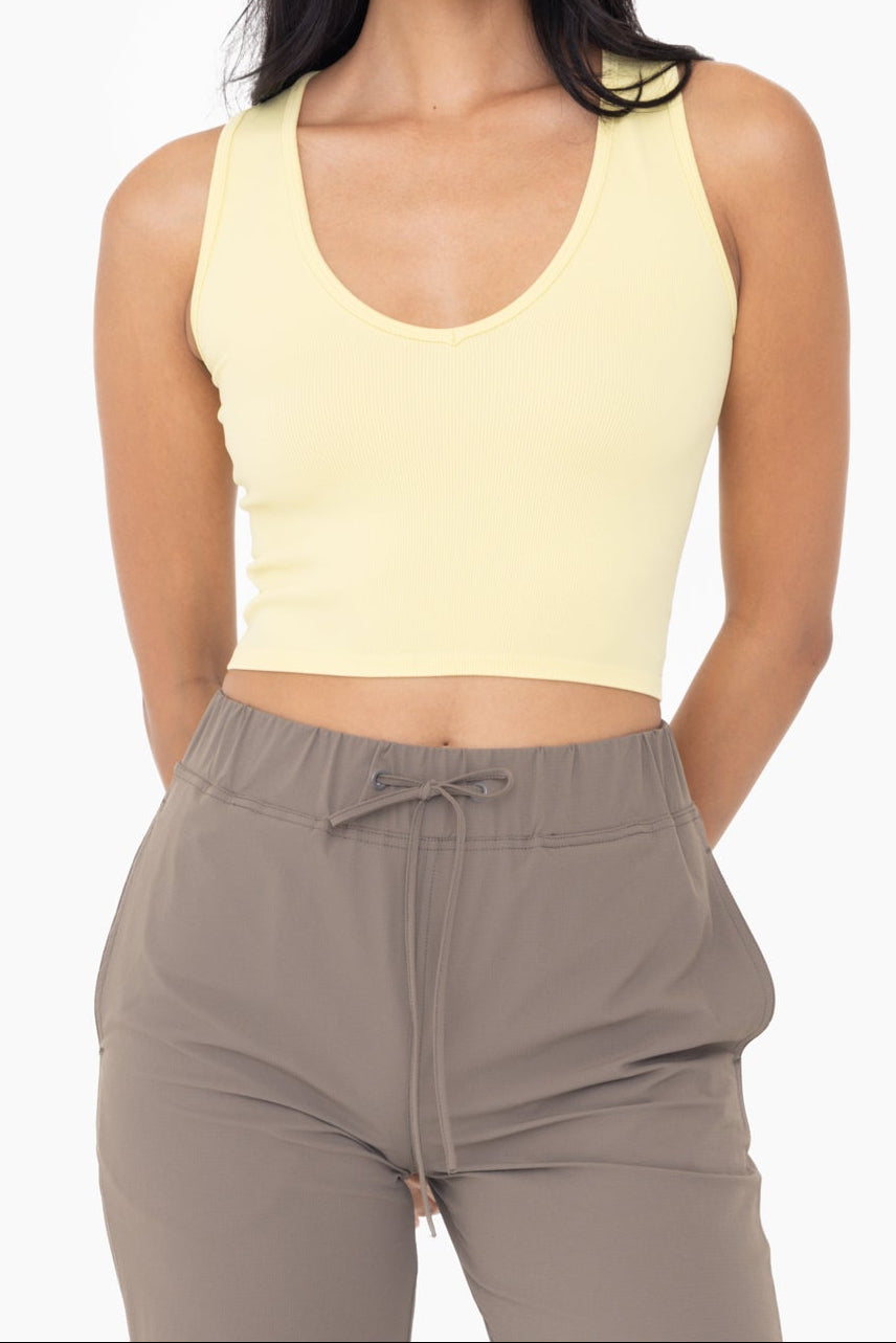 A woman wearing a yellow ribbed v-neck crop top and gray trousers.