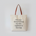 A beige canvas tote bag with brown leather handles.